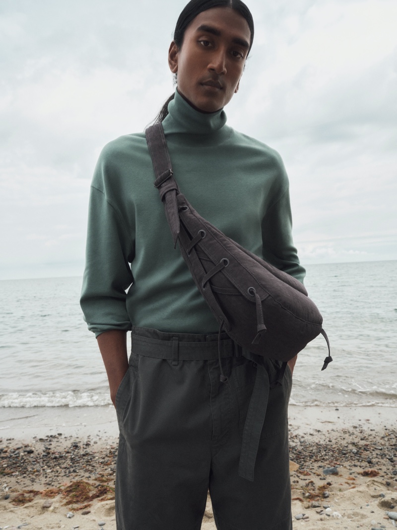 Taking hold of a small soft game shoulder bag, François Delacroix wears a cotton jersey turtleneck top with straight leg canvas pants from the LEMAIRE x Mytheresa collection.