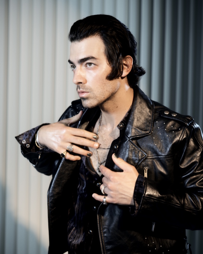 Singer Joe Jonas wears a cropped leather biker jacket and velvet western shirt by Saint Laurent. Jonas accessorizes with an Alexander McQueen necklace, Maple ruby ring, and Bleue Burnham sapphire ring.