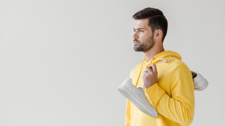 man yellow hoodie holding white sneakers