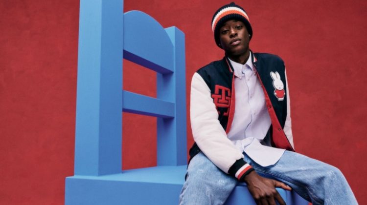 Sitting on an oversized chair, Babacar N'Doye sports a varsity jacket, knit beanie, and jeans from the Tommy Hilfiger x Miffy collection.