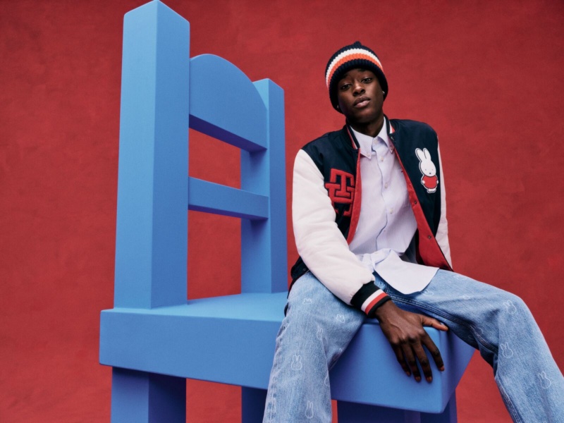 Sitting on an oversized chair, Babacar N'Doye sports a varsity jacket, knit beanie, and jeans from the Tommy Hilfiger x Miffy collection.