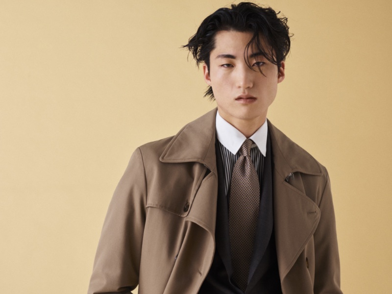 Young Woong Kim dons a brown trench over a classic suit look from Canali's fall-winter 2023 collection.
