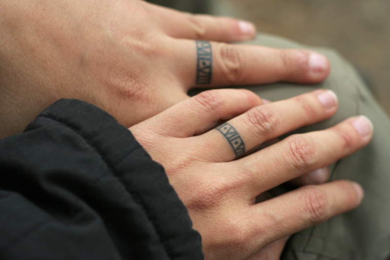 A couple shows off matching tattoos on their ring fingers. 