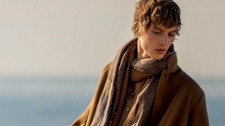 Leon Dame dons a light scarf with a brown jacket and white jeans for Loro Piana's spring-summer 2023 campaign.