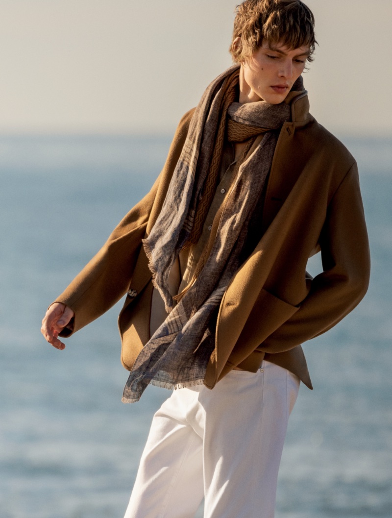 Leon Dame dons a light scarf with a brown jacket and white jeans for Loro Piana's spring-summer 2023 campaign.