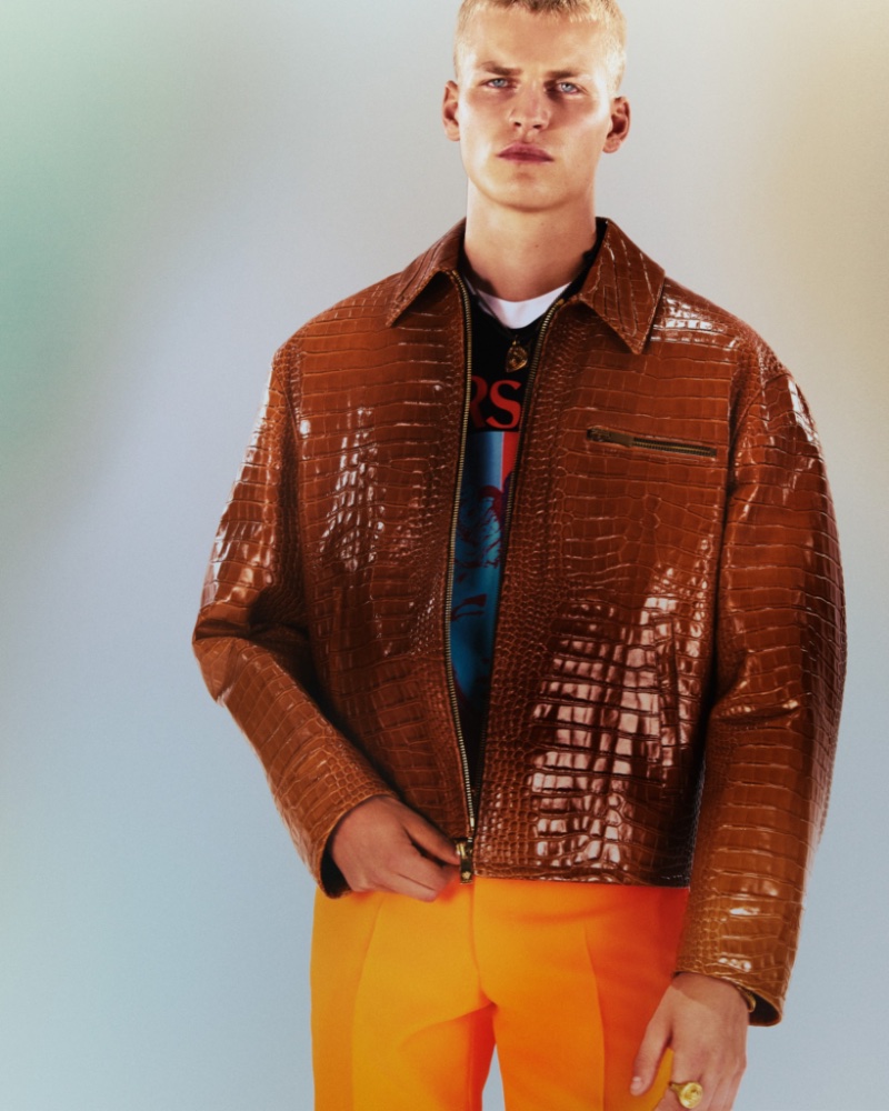 Wearing a brown leather jacket with orange trousers, Timo Pan fronts Versace’s resort 2023 men’s campaign.