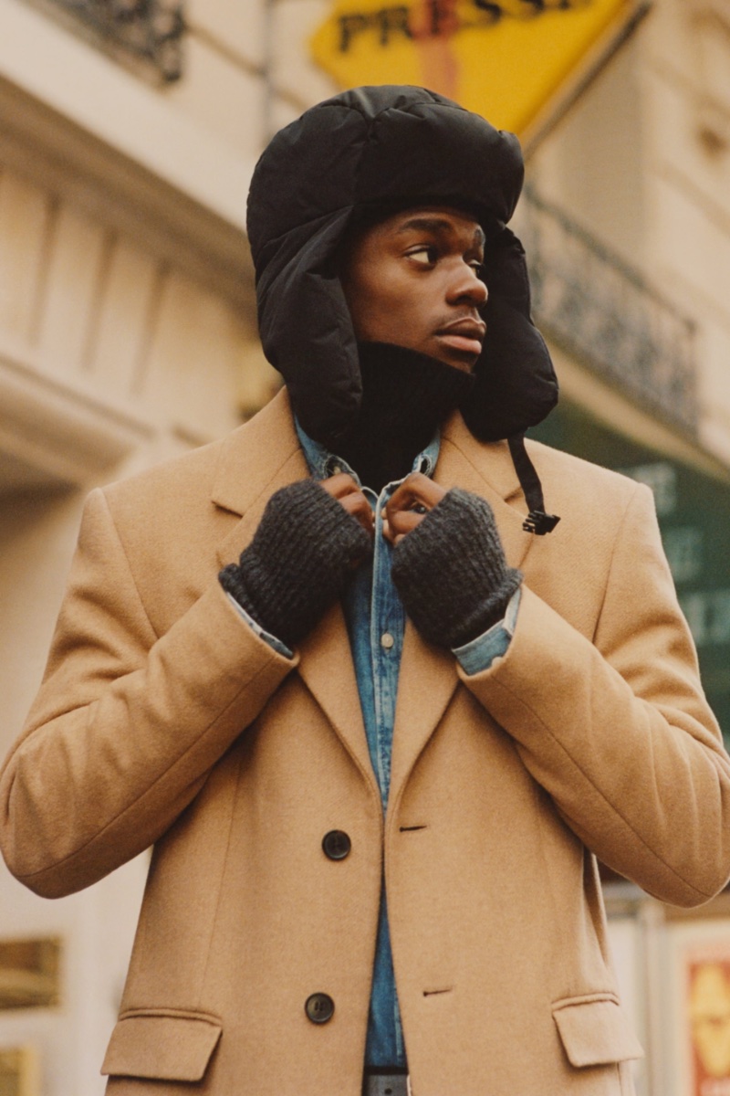 Henry Makuntima sports a stretch camel coat over a denim shirt with a trapper hat.