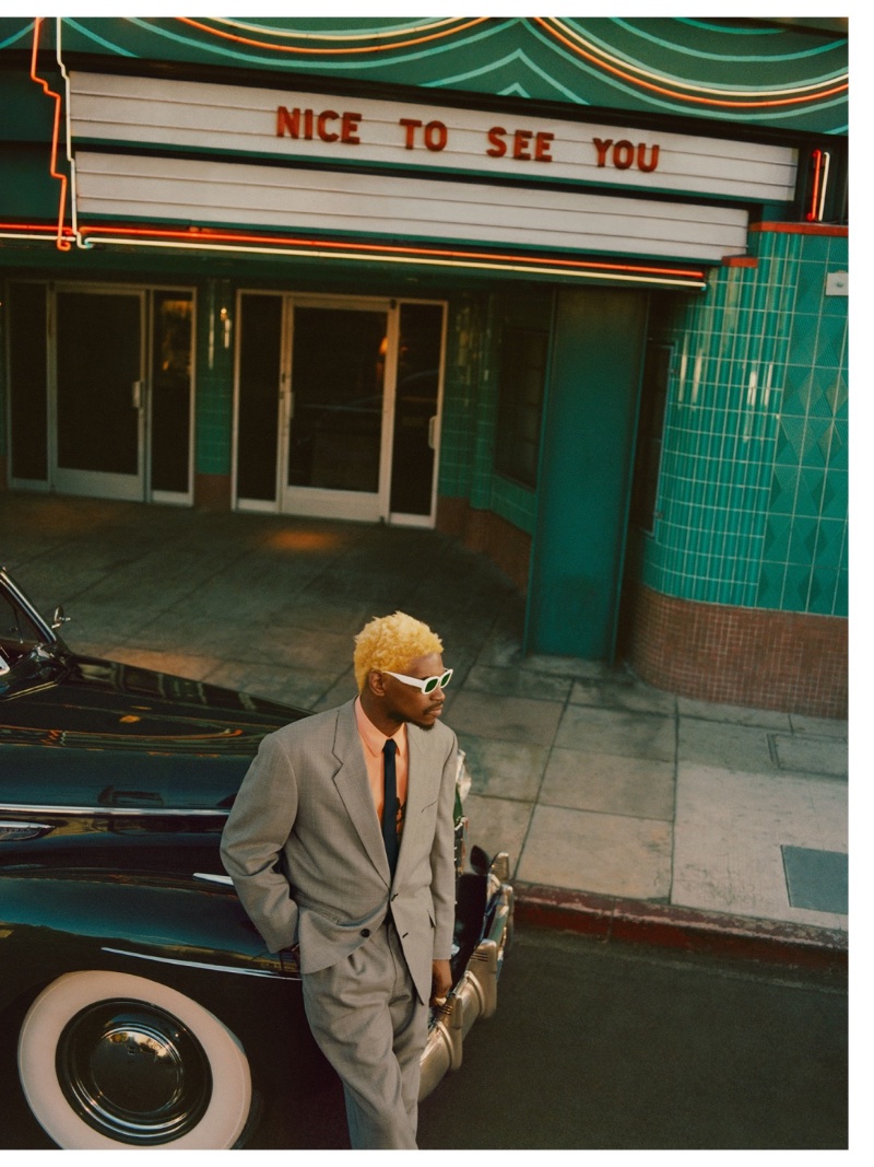 Posing outside a theater in a dapper gray suit, A$AP Nast sports his Warby Parker Cloud White NST2-002 sunglasses.