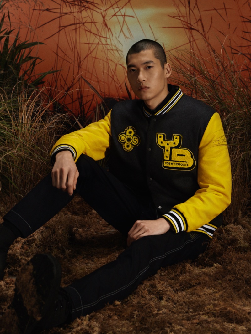 Yun Hoseok embraces collegiate style in a yellow and black varsity jacket from the COS x YEBOAH Metamorphosis collection. 