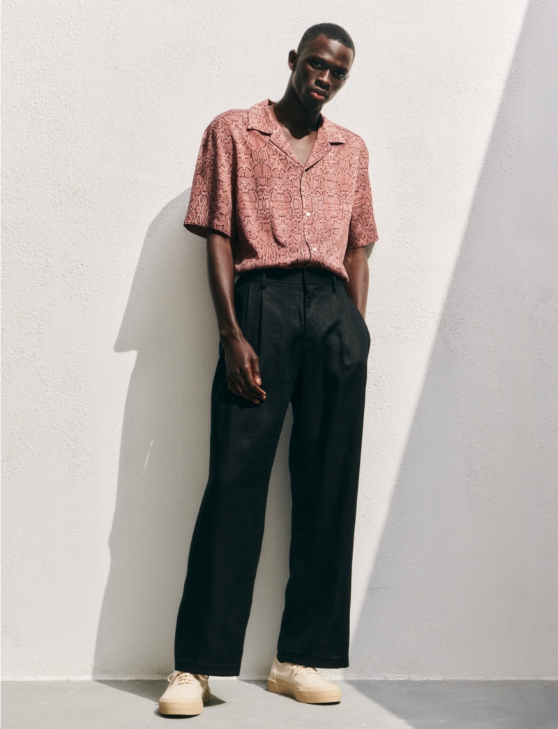 H&M unveils early summer 2023 styles, enlisting model Khadim Sock, who wears a regular-fit reptile print short-sleeve shirt with pleated trousers.