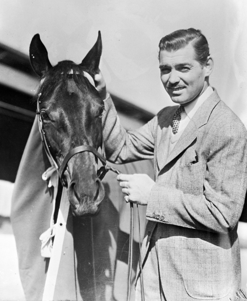 Clark Gable wears a light-colored suit with a v-neck sweater as he poses with his horse Beverly Hills at his ranch circa April 21, 1937.