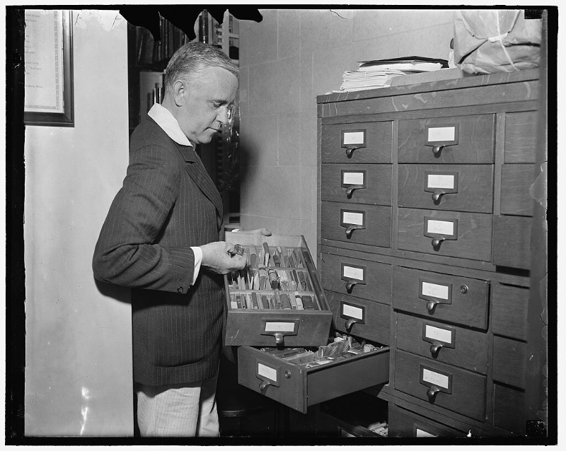 Mixing a light and dark pinstripe suit jacket and pants, Library of Congress Rare Book Division curator V. Valtra Parma handles a collection of miniature books circa 1937.