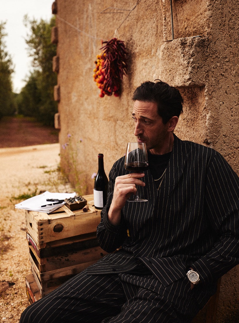 Enjoying a glass of wine, Adrien Brody wears a pinstripe outfit for Kith's summer 2023 campaign. 