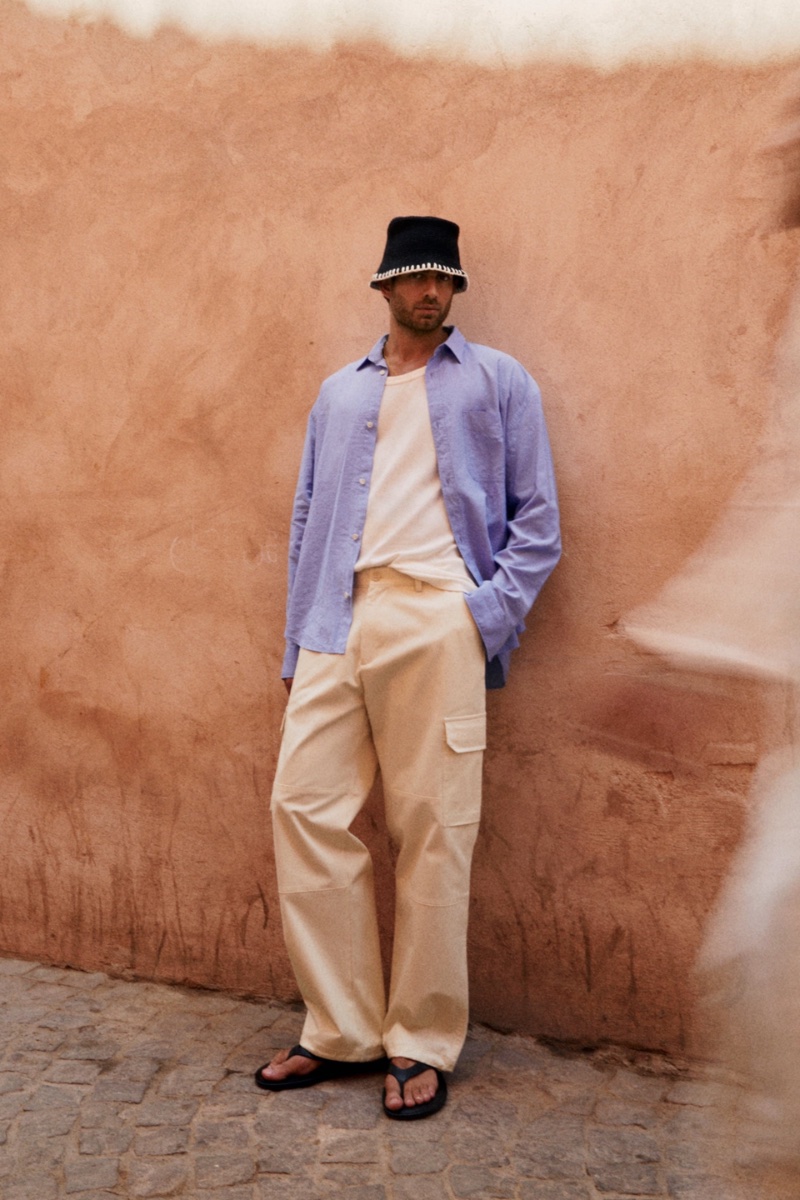 In front and center, Andrew Georgiades rocks a Zara fluid pocket shirt, ribbed tank top, straight cargo pants, and leather sandals. 