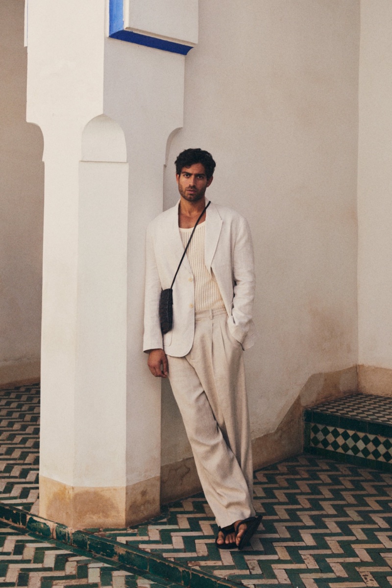 Andrew Georgiades models a Zara linen blazer and trousers with a crochet tank, leather sandals, and a crossbody bag. 