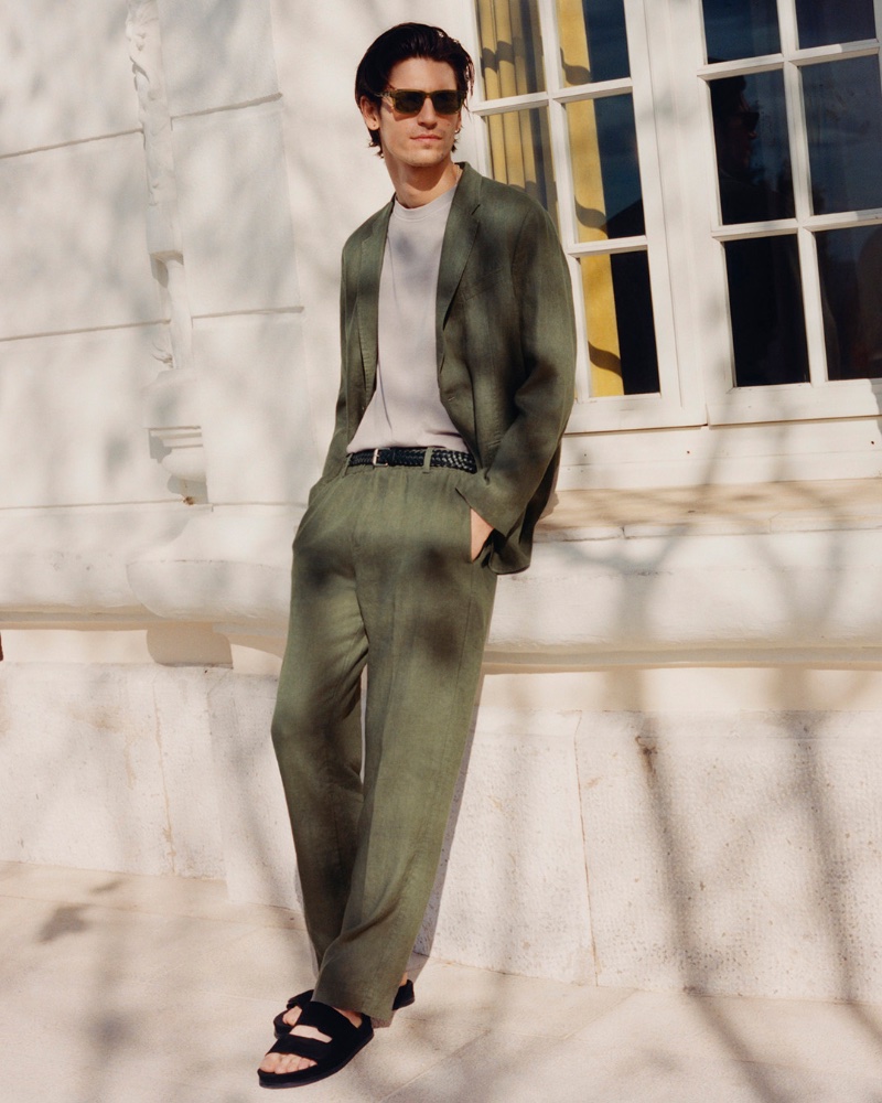 Reuniting with COS for summer, Justin Eric Martin wears an unstructured linen suit with a t-shirt, suede slide sandals, and square-frame sunglasses.