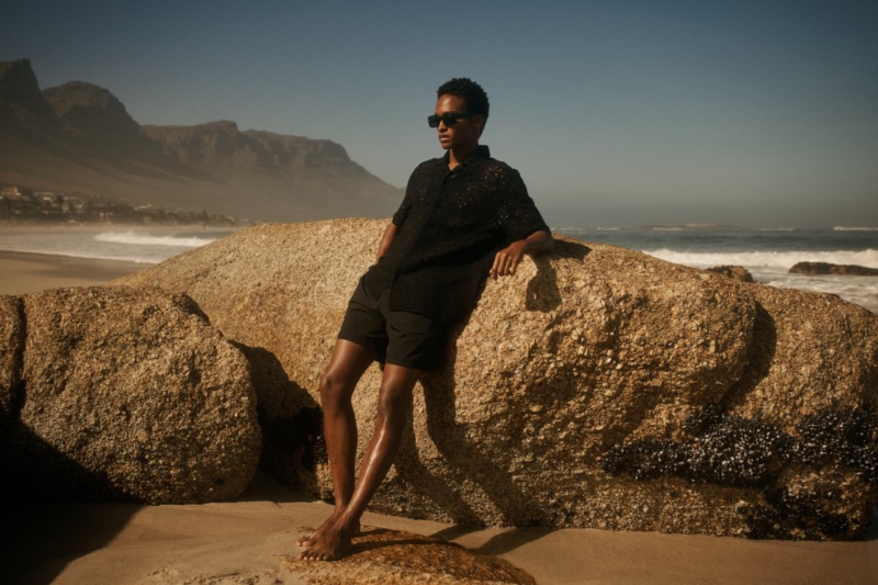 It's all about monochromatic style as Stan Taylor hits the beach in a black crochet short-sleeve shirt and swim shorts.