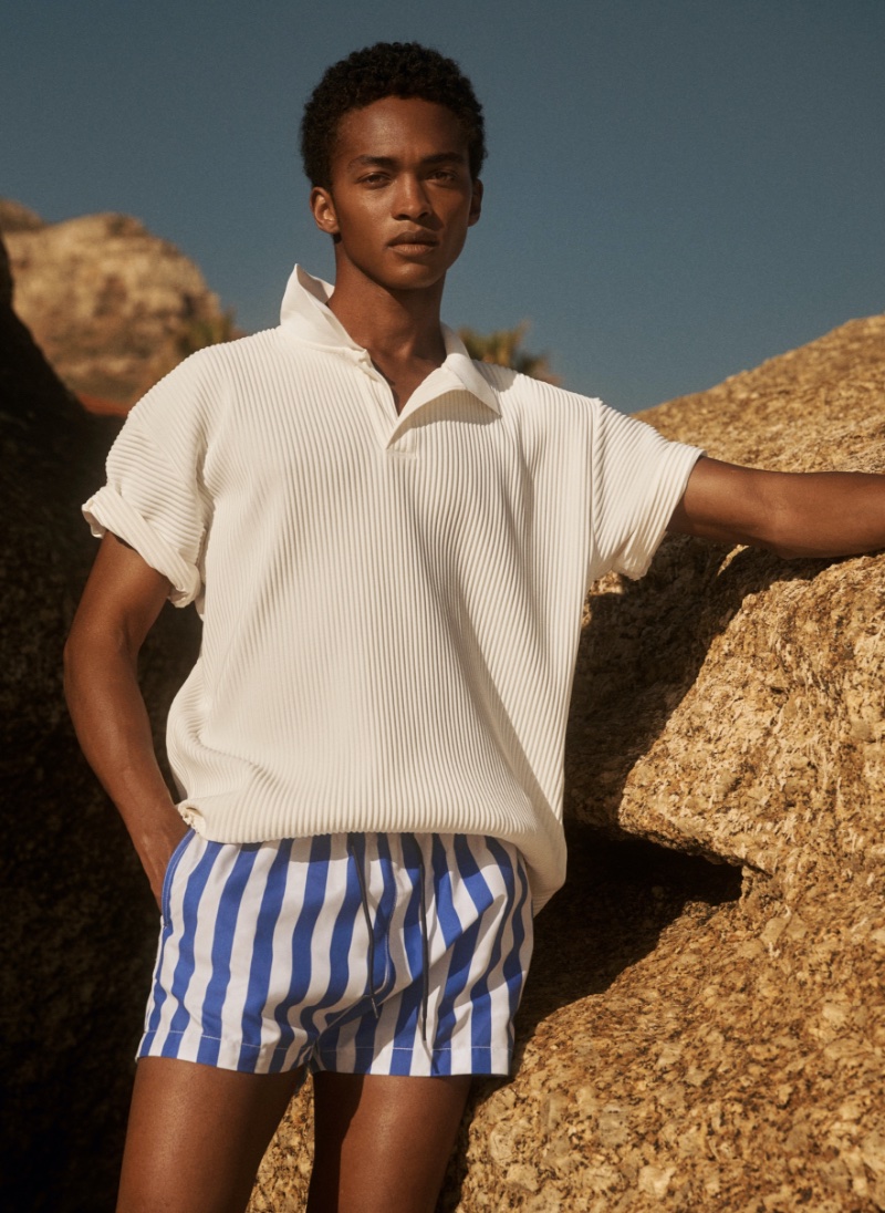 Making a textured statement, Stan Taylor rocks a relaxed-fit pleated polo shirt with striped blue and white swim shorts.