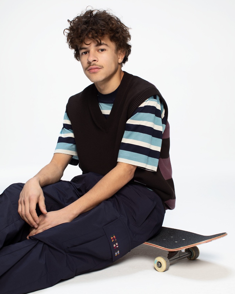 Logan Da Silva Ortiz sports a knit vest with a blue stripe pocket t-shirt and navy cargo trousers from the Paul Smith + Pop Trading Company capsule collection. 