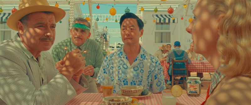 Liev Schreiber wears a seersucker suit as J.J. Kellogg opposite Steve Carell's motel manager and Stephen Park as Roger Cho in Wes Anderson's Asteroid City. Park wears a resort-style Cuban-collar short-sleeve shirt for the film scene.