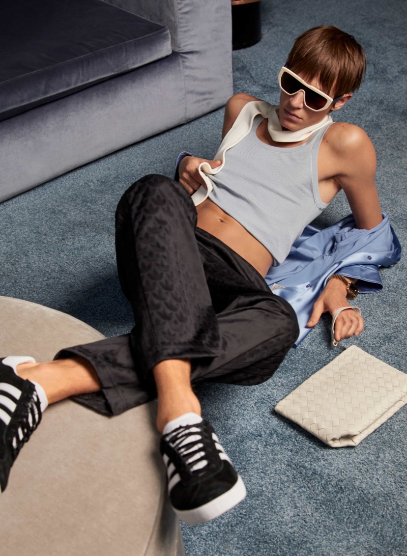 Model Michael Zieliński relaxes in a tank and Adidas Originals monogram track pants with Adidas Originals Gazelle 85 sneakers $130. He's pictured alongside a Bottega Veneta beauty case $795. 