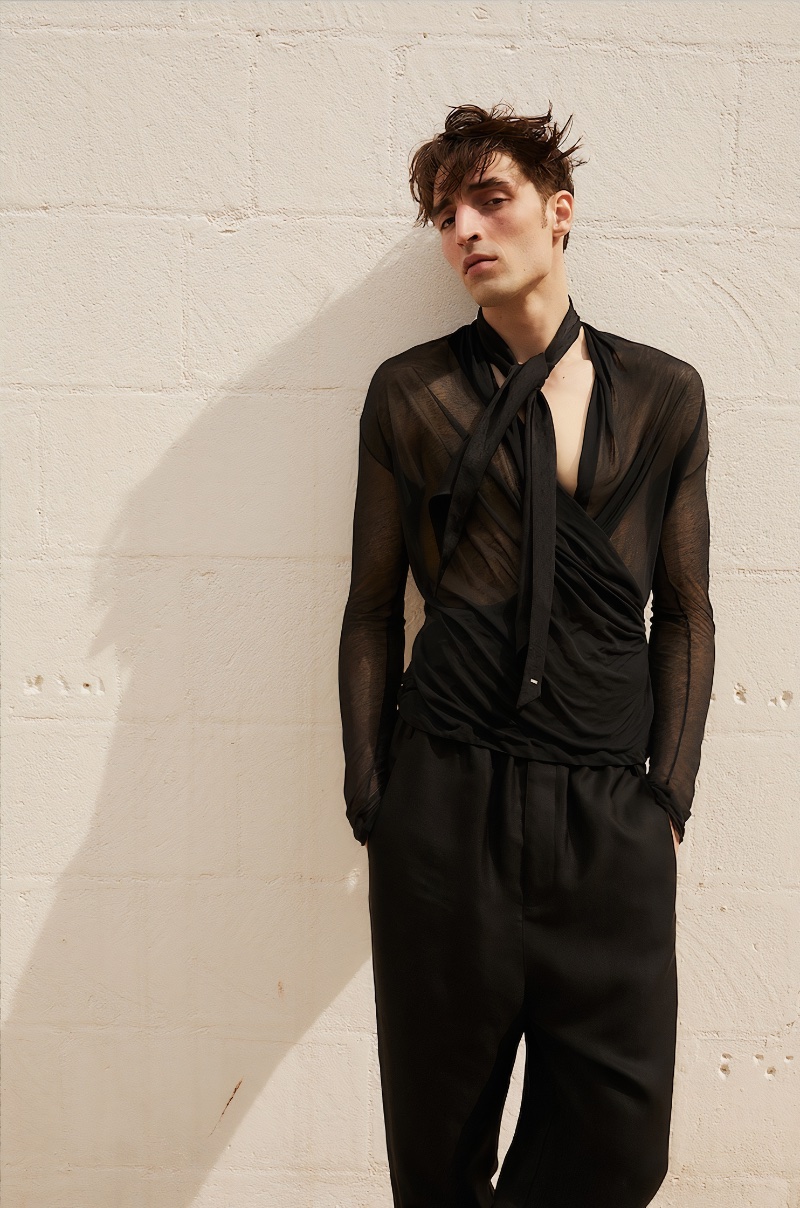 Wearing all black, Luca Jamal models a Saint Laurent cardigan with high-waist baggy pants and a Levalliere logo silk scarf.