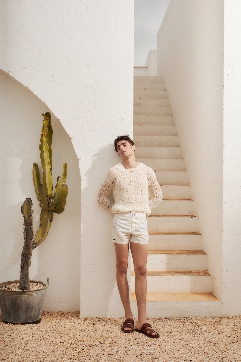 Luca Jamal wears an Isabel Marant open knit sweater with Sundek swim shorts, Ferragamo leather sandals, and an Alighieri pendant necklace.