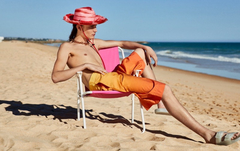 Louis Joseph hits the beach with YOOX, wearing a Sensi Studio straw Panama hat, Balenciaga rubber slides, and orange gradient shorts.