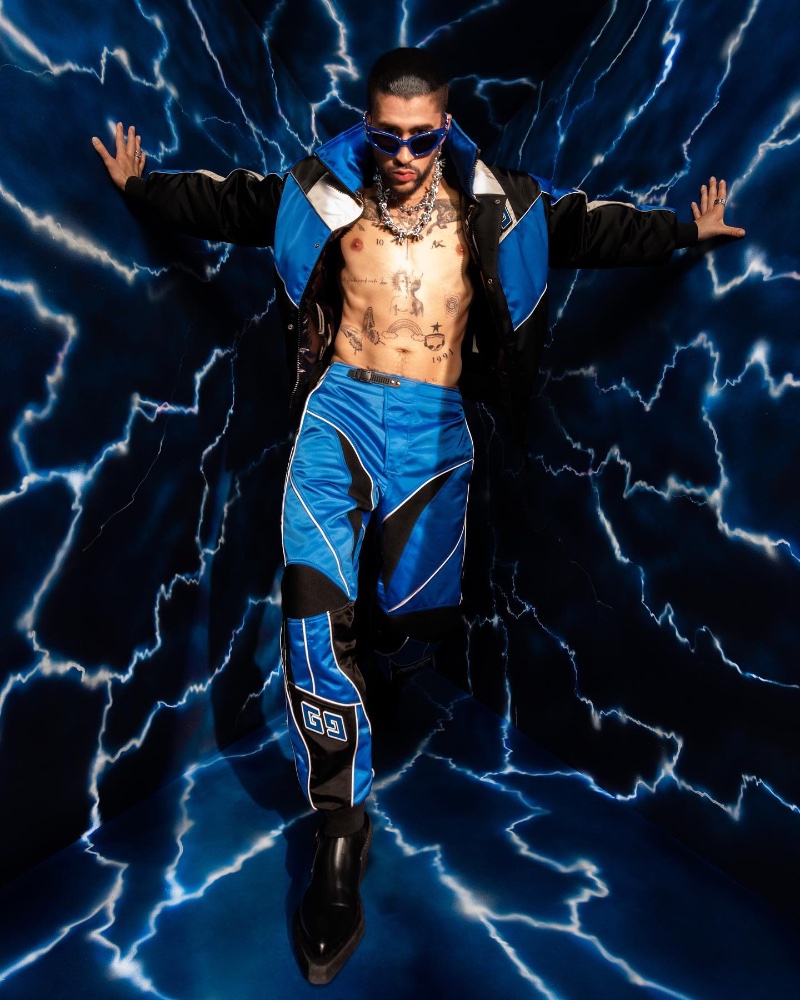 Making an electric statement, Bad Bunny rocks a Heliot Emil jacket and pants with Gentle Monster Paso BL3 sunglasses. He also sports Louis Vuitton shoes and Apt.1007 necklaces.