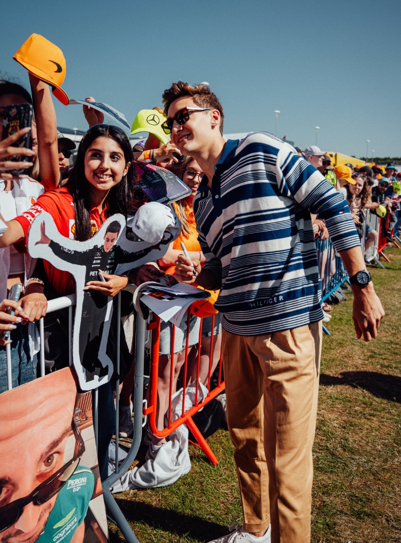 Grand Prix winner George Russell sports a Tommy Hilfiger oversized striped long-sleeve polo with trousers and white sneakers. 