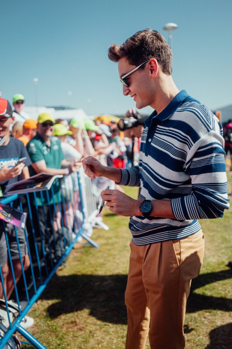 Signing autographs for fans, George Russell embraces an all-American aesthetic in a Tommy Hilfiger outfit. 