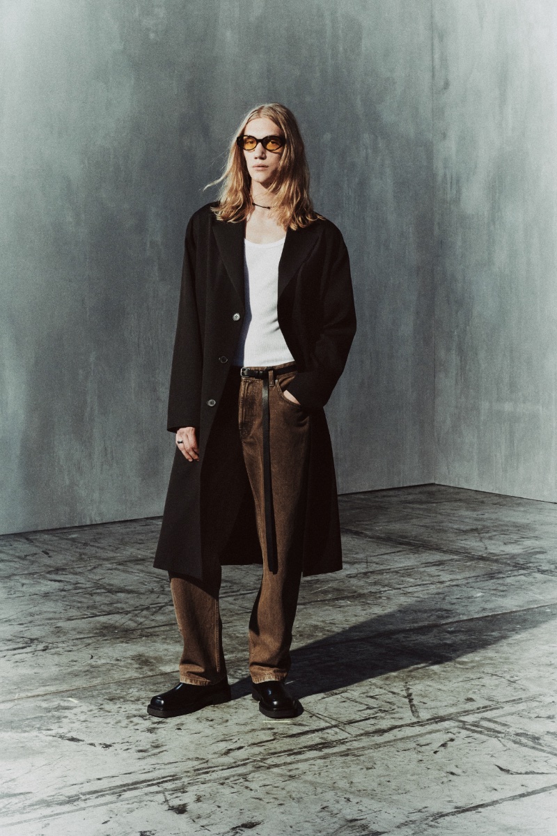 Valentyn Boiko wears a wool coat with waxed effect jeans, square toe leather Chelsea boots, and oval sunglasses from the Zara Edition fall 2023 collection. 