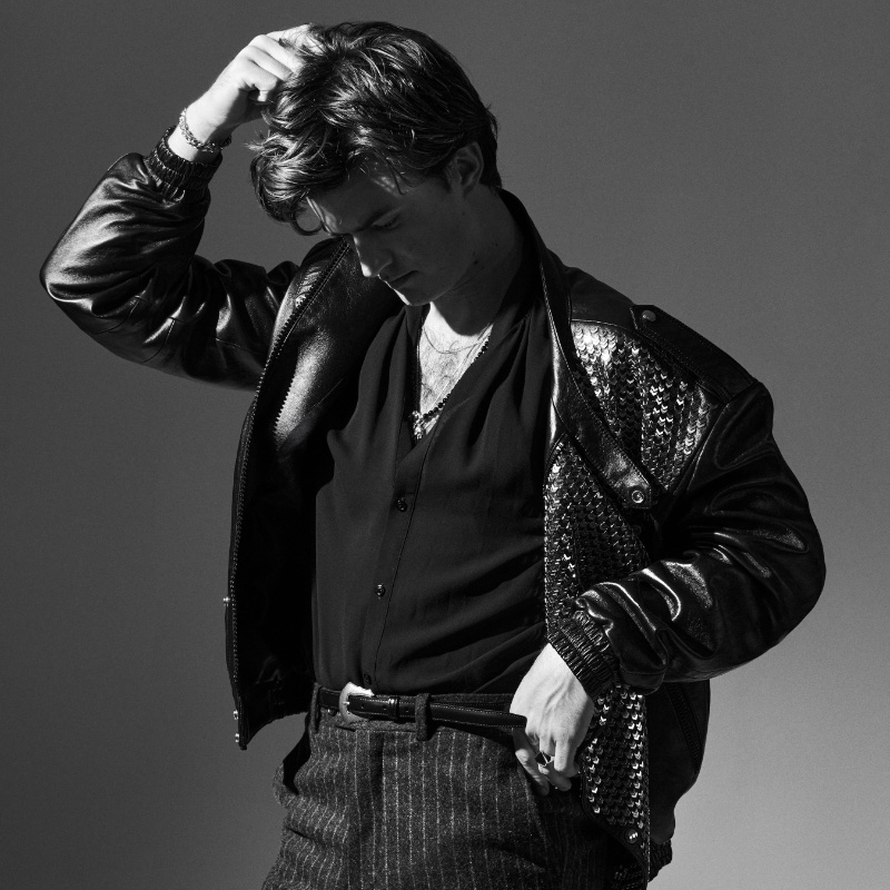 Appearing in a new photoshoot, Joe Keery sports a Celine jacket and belt with a Willy Chavarria shirt and Bally trousers. 