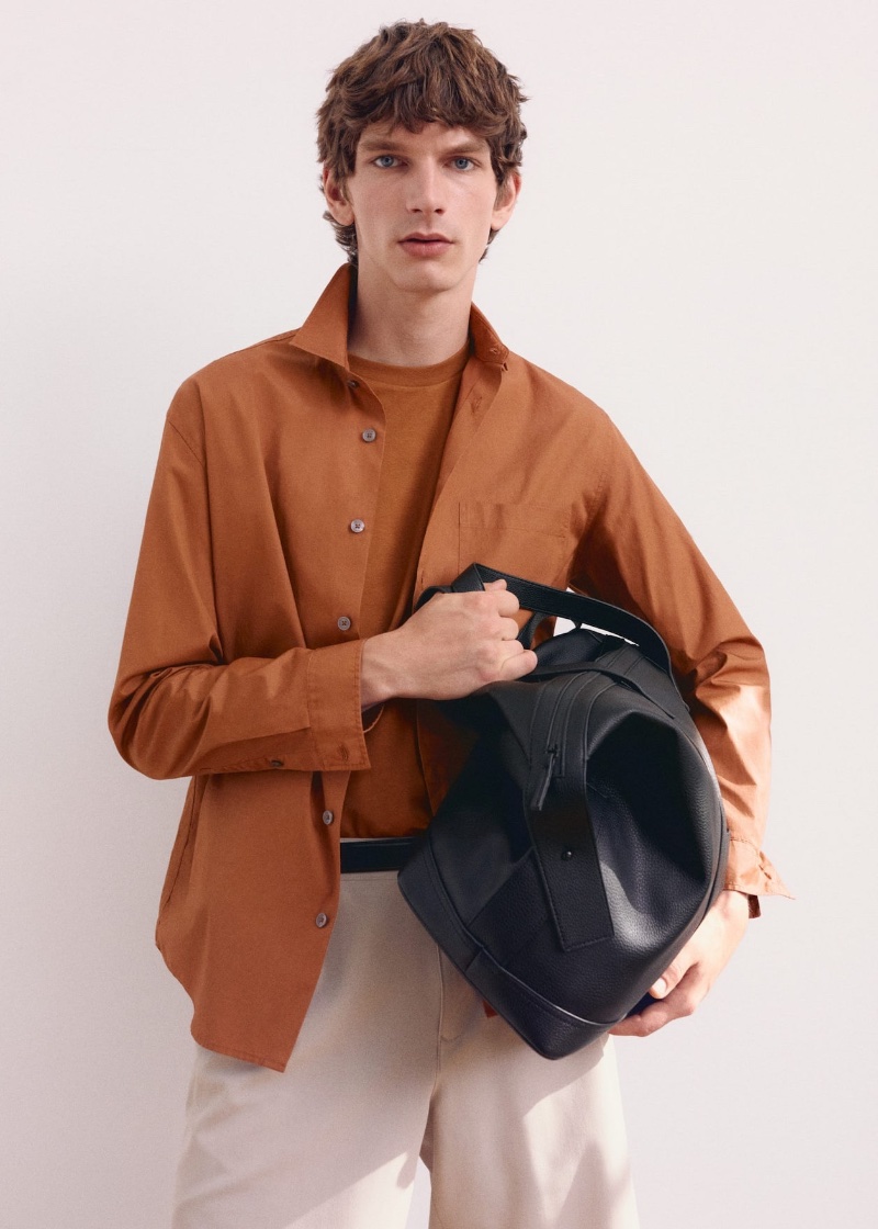 Taking hold of a bowling bag, Erik van Gils wears a brown shirt over a pocket tee by Mango.