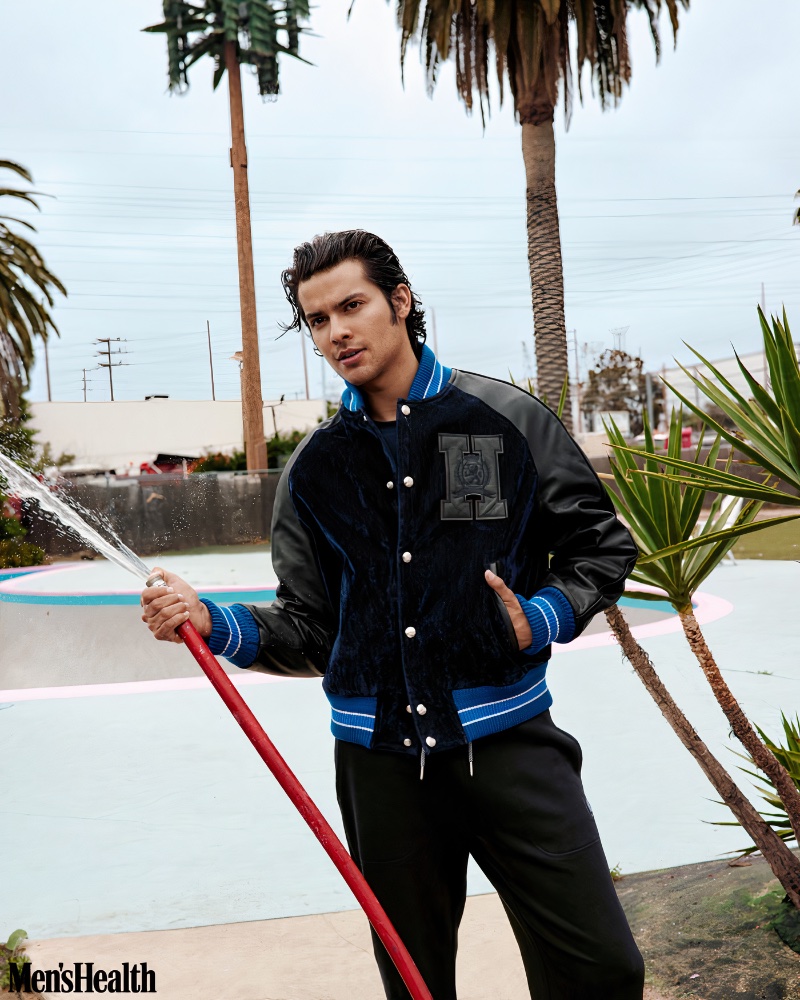 Xolo Maridueña wears a Tommy Hilfiger varsity jacket with a Bugatchi t-shirt and Armani Exchange pants. 