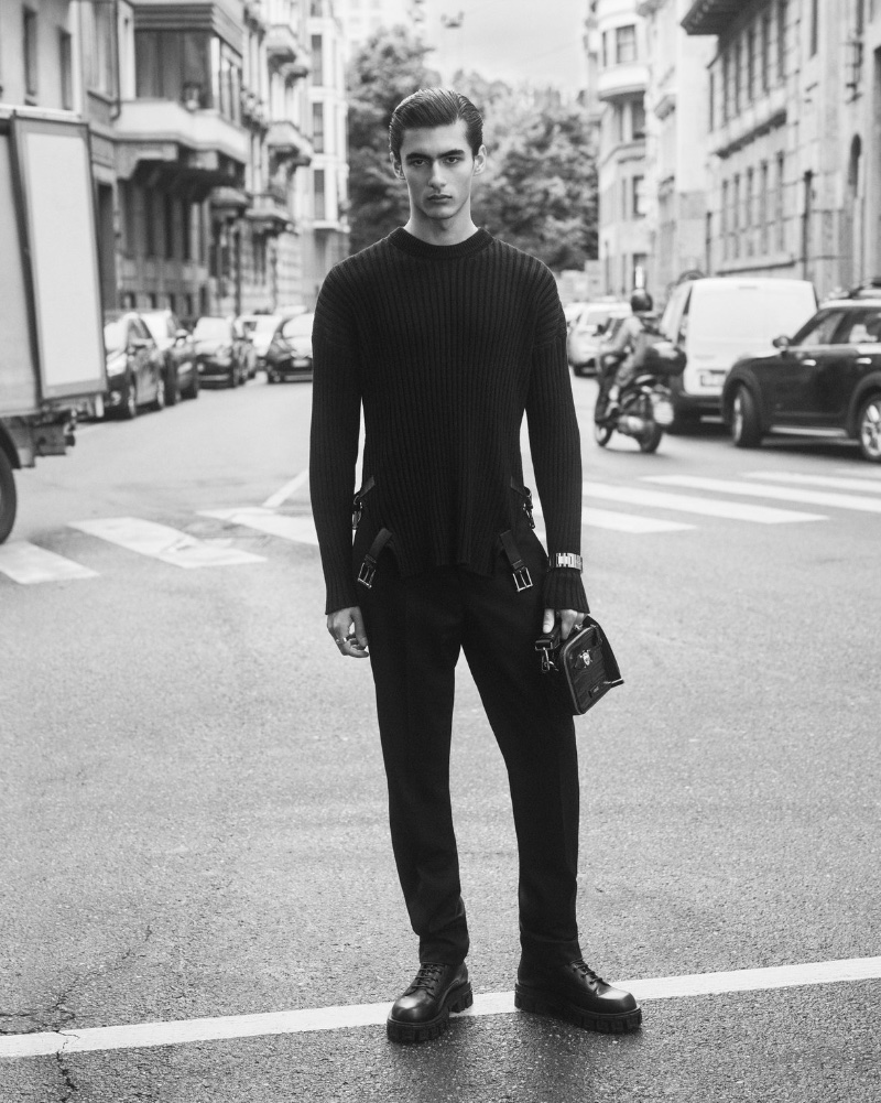 Akbar Shamji models a ribbed black sweater with jeans for Versace's fall-winter 2023 denim campaign.