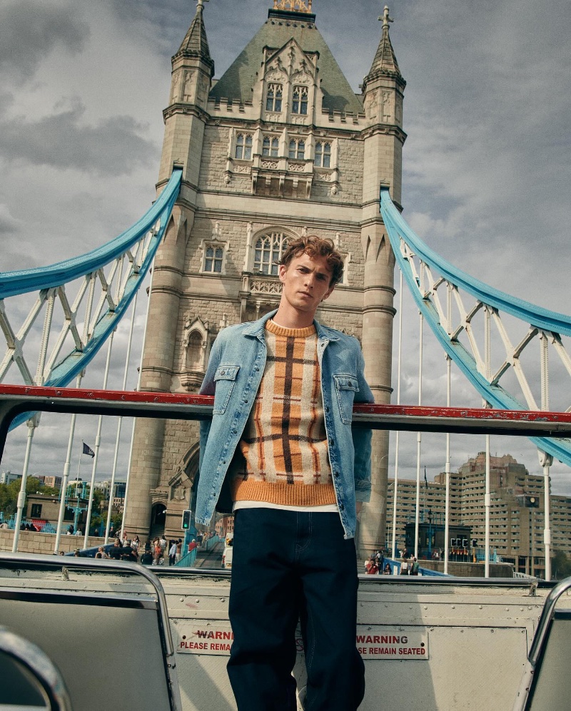 Donning a jean jacket over a check sweater, Luc Defont-Saviard poses against a backdrop of the Tower Bridge in London for Pepe Jeans' fall-winter 2023 campaign. 