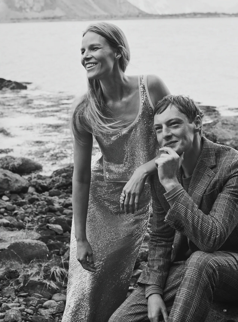 Roberto Sipos, seated in sartorial splendor, shares a moment of joy with a fellow model against the scenic seaside, celebrating the holidays with Banana Republic.
