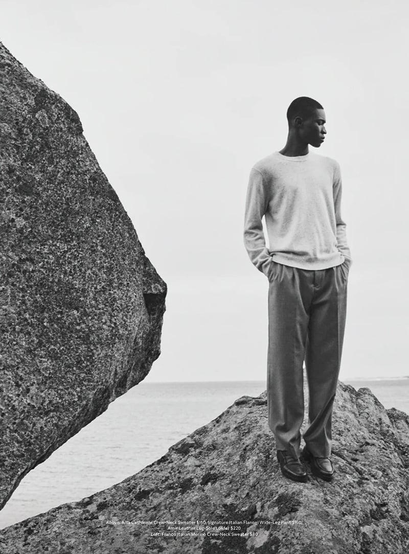 Kwaku Ansong stands poised on a rock, his gaze contemplative, wearing a soft cashmere sweater. 