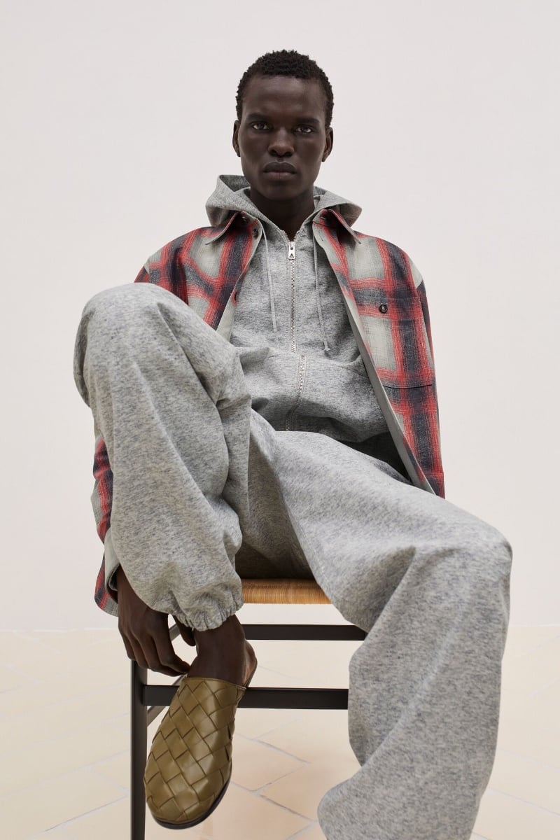 Badhiel Lony Nyang exudes relaxed sophistication in a heather grey hoodie and matching joggers, layered under a red plaid jacket, finished with Bottega Veneta's signature woven leather slides.