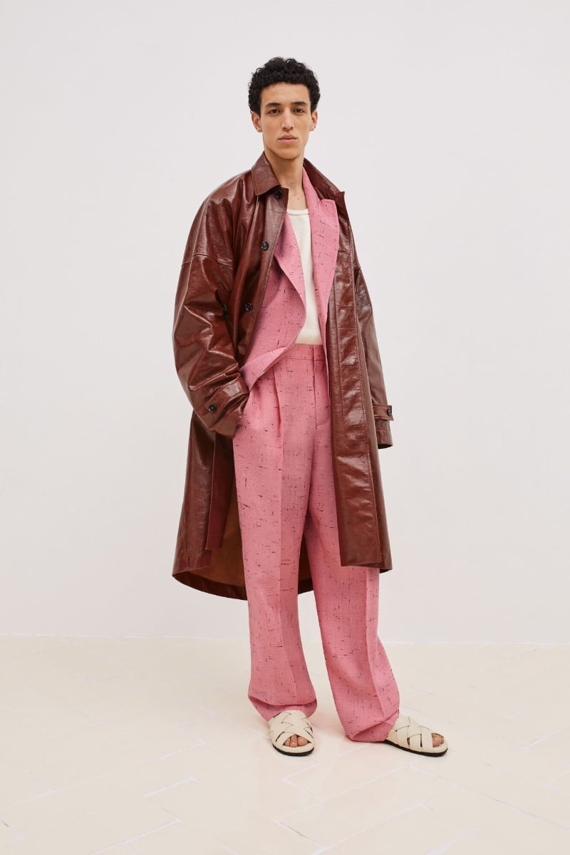 Walid Fiher presents a contemporary Bottega Veneta look, pairing a glossy oxblood trench coat with a textured pink suit, complemented by minimalist cream sandals.