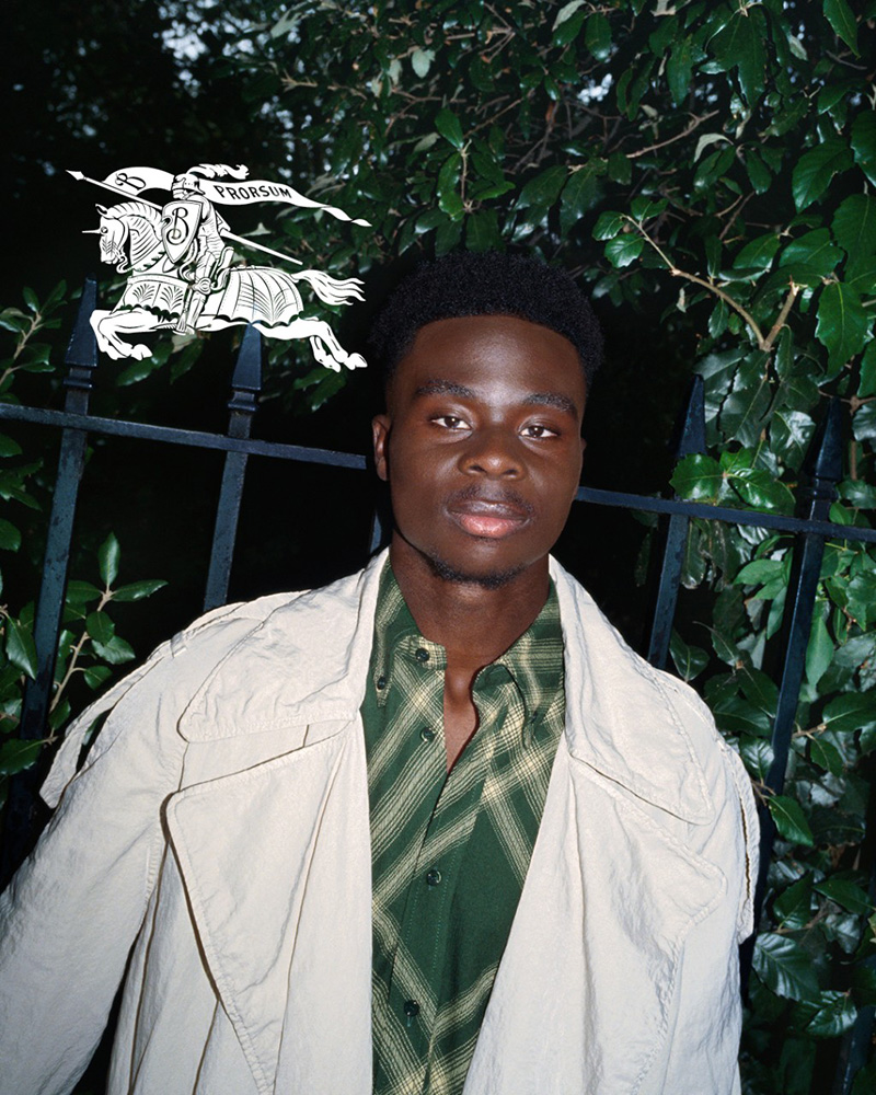 Bukayo Saka exudes relaxed confidence in a Burberry trench coat over a plaid green shirt for Burberry's spring 2024 campaign. 