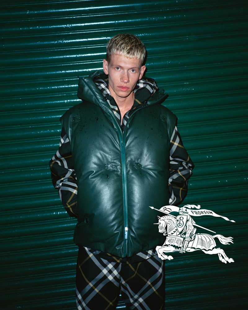 Slew stands boldly in a sleeveless puffer jacket against a striking green backdrop, channeling the youthful energy of Burberry's spring 2024 collection.