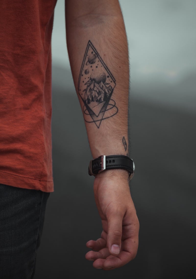 This forearm tattoo artfully combines a serene landscape with an ethereal celestial body, suggesting a cosmic connection.