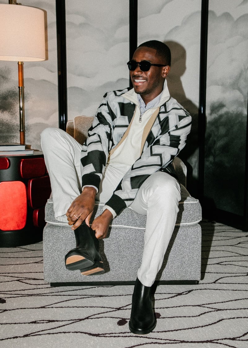 For dinner, Damson Idris pairs a reversible bomber with a stand collar sweater and pleated trousers, grounded by sleek leather Chelsea boots by Tommy Hilfiger. 