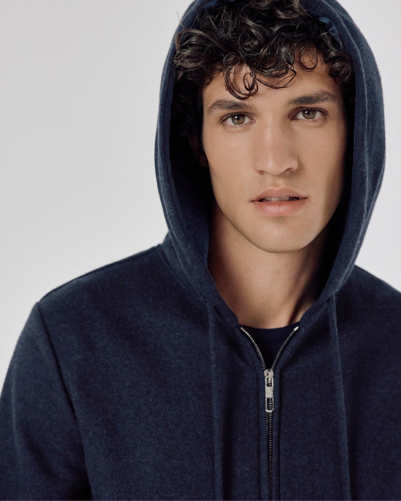 Francisco Henriques showcases urban allure in a navy zip-up hoodie, with the hood draped softly around his tousled curls.