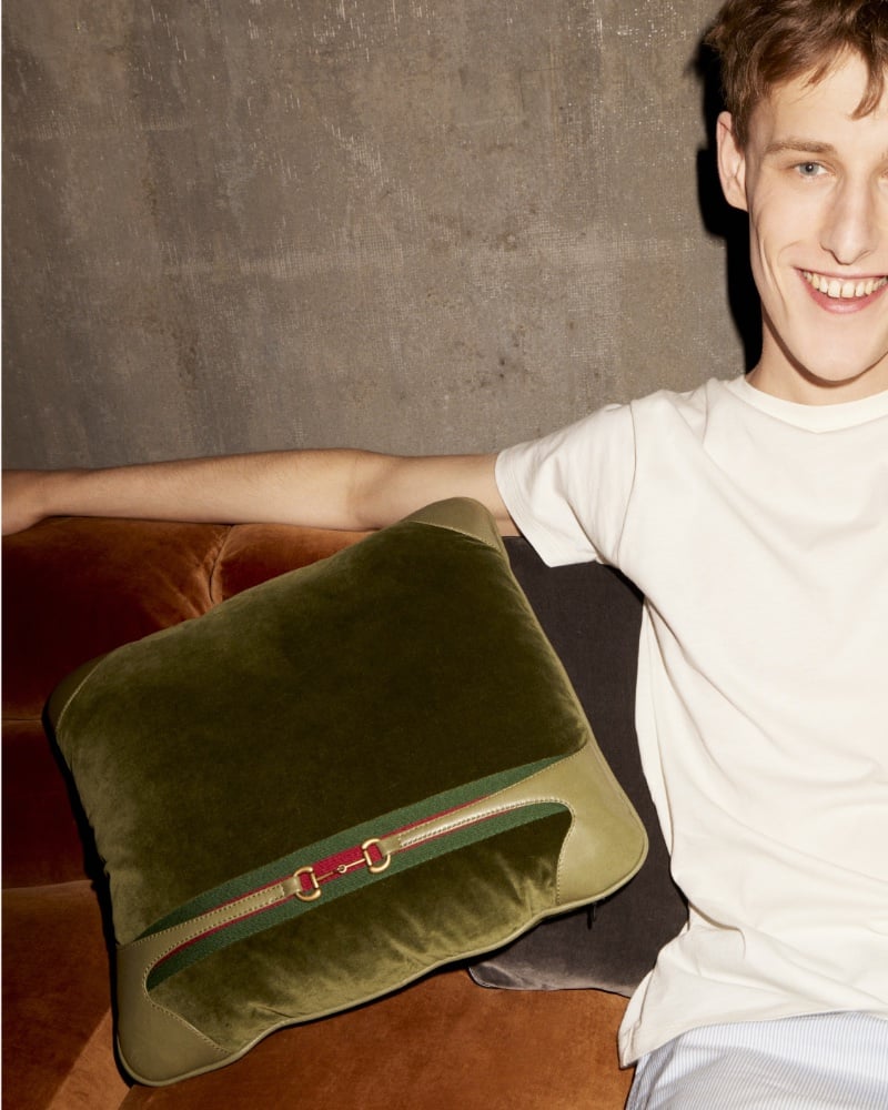 A playful grin from Felix Edwards and a plush Gucci pillow, a blend of comfort and luxury.