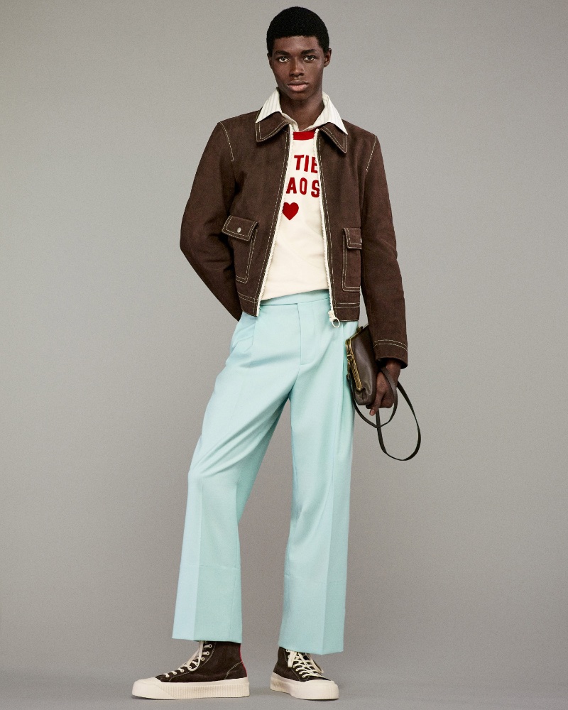 Zaram Obasi cuts a striking figure in a Harry Lambert for Zara Cutie Chaos suede jacket and ice blue trousers, complemented by a collared shirt and graphic tee.