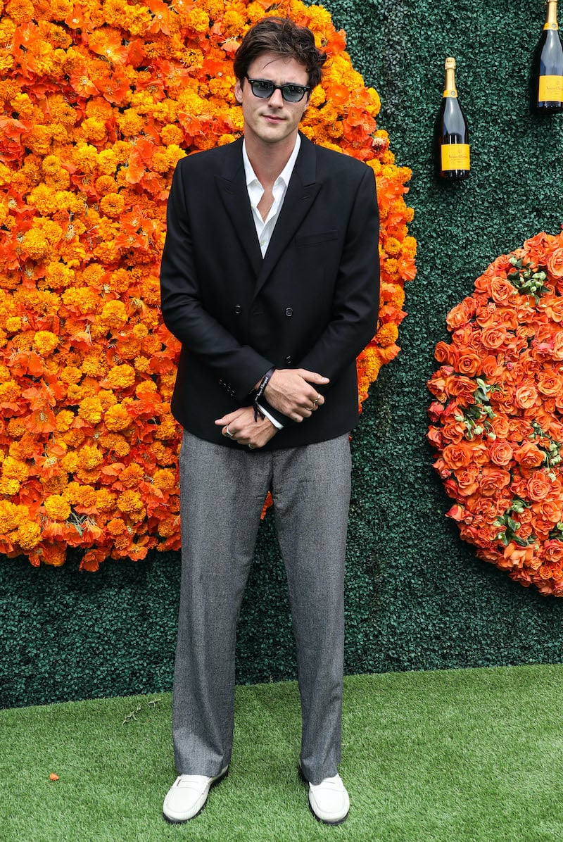 Jacob Elordi brings classic Hollywood charm to the Veuve Clicquot Polo Classic, pairing a crisp double-breasted black jacket with relaxed grey trousers, offset by casual white loafers, and finishing the look with timeless sunglasses—a perfect blend of traditional tailoring and laid-back elegance.