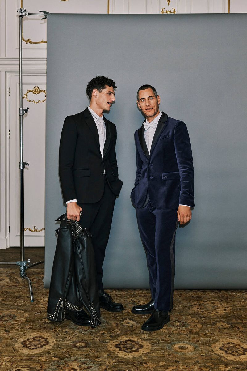 Pau Ramis and Axel Hermann exude sophistication in conversation, with Pau in a sharp Karl Lagerfeld black suit and Axel in a luxurious navy velvet tuxedo. 